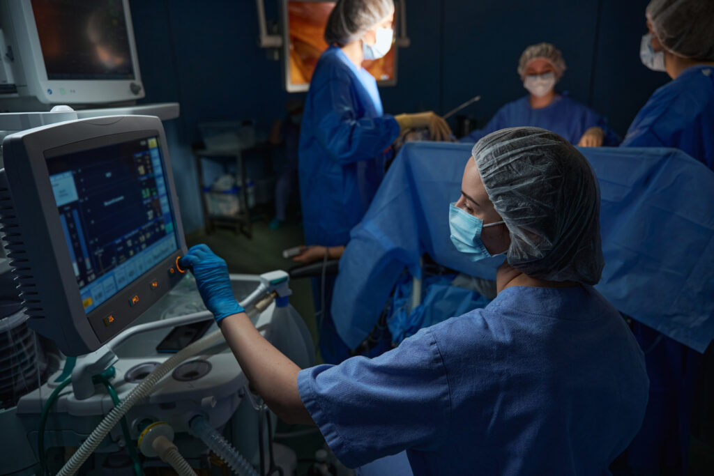 Nurse in protective mask near the screen of the artificial lung ventilation equipment. Laparoscopy in surgery