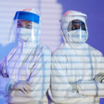 Medium shot of diverse man and woman laboratory technicians in white hazmat suits and face shields standing shoulder to shoulder while looking at camera